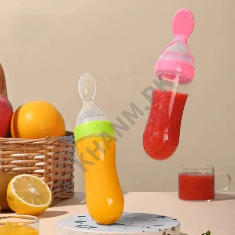 Orange baby bottle and pink fruit feeder with fruits and juice on a table